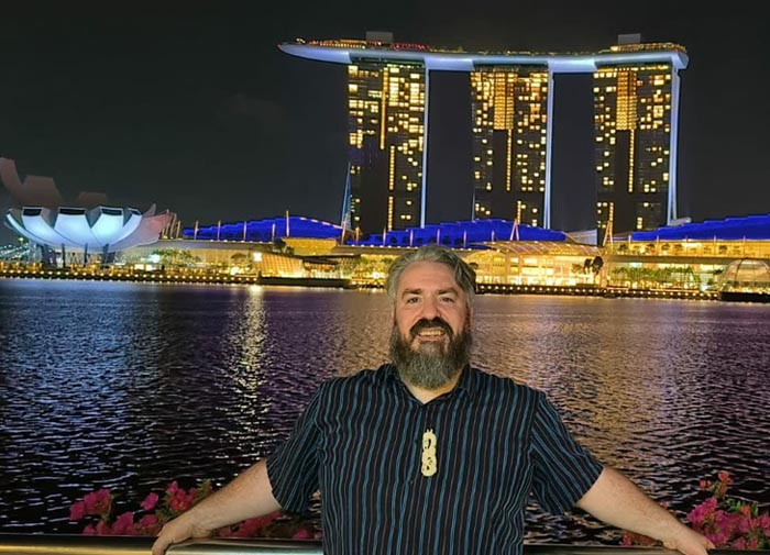 Neil Wallace in front of a large building in Singapore, lit up during the evening when lighting lights feature across the harbour